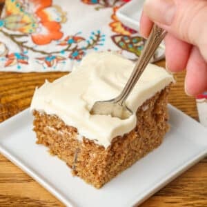 A fork plunges into the cream cheese frosting on top of spice cake in this vertically aligned image.
