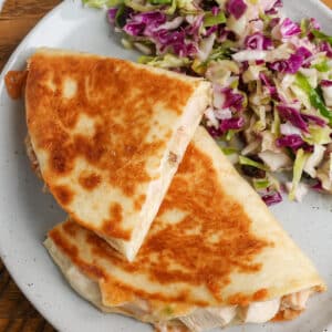 A top down photo of a quesadilla on a white plate over a wooden tabletop.