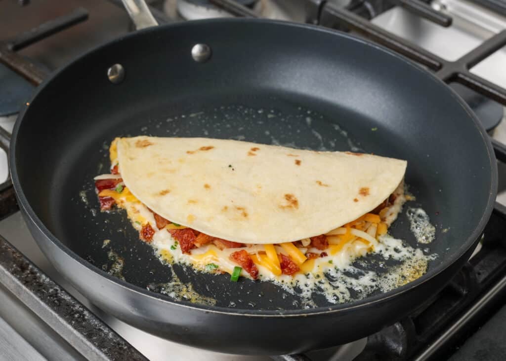 The quesadilla has been folded over and is ready to flip in the pan.