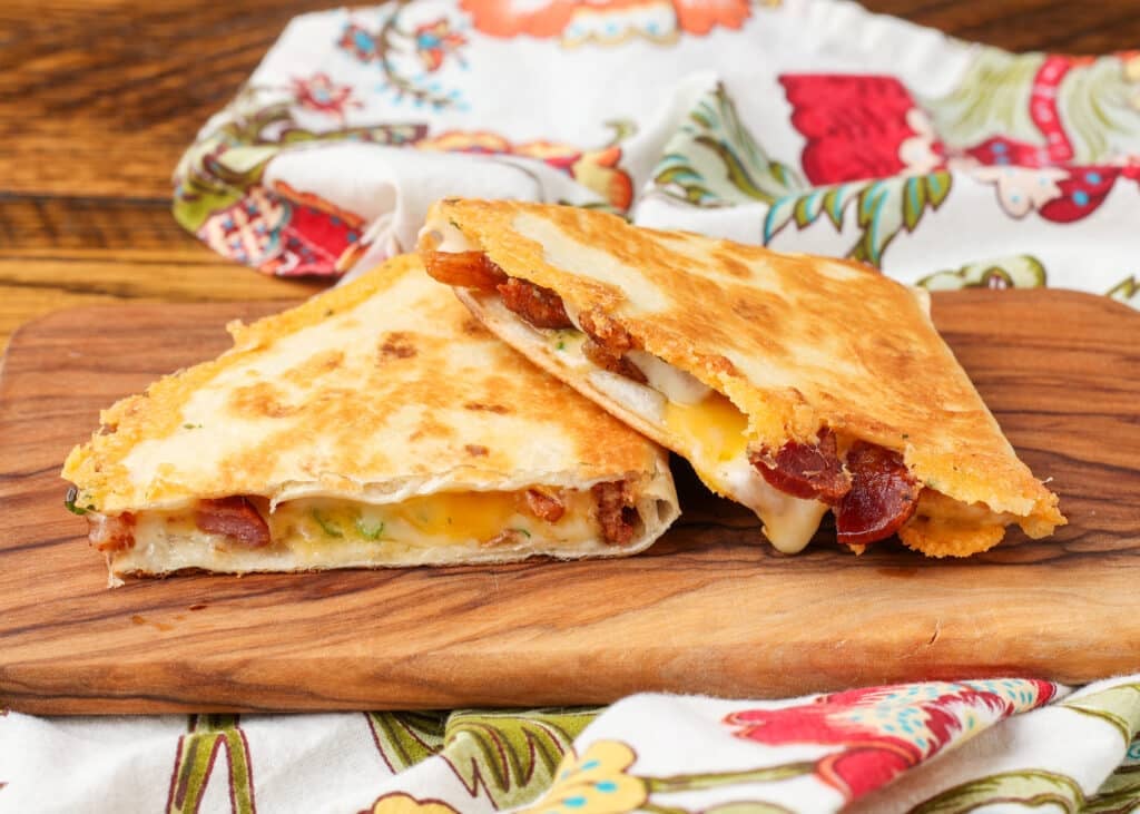 a bacon quesadilla sliced on a wooden serving platter with a tea towel in the background