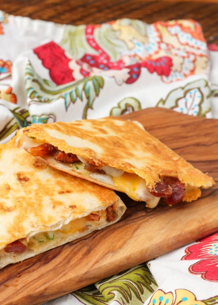 A vertically aligned photo of bacon quesadilla triangles  ready to eat on a serving tray.