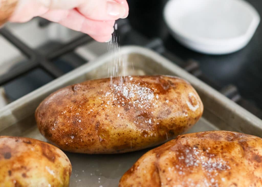Sprinkling salt over the oiled potatoes on a baking sheet.