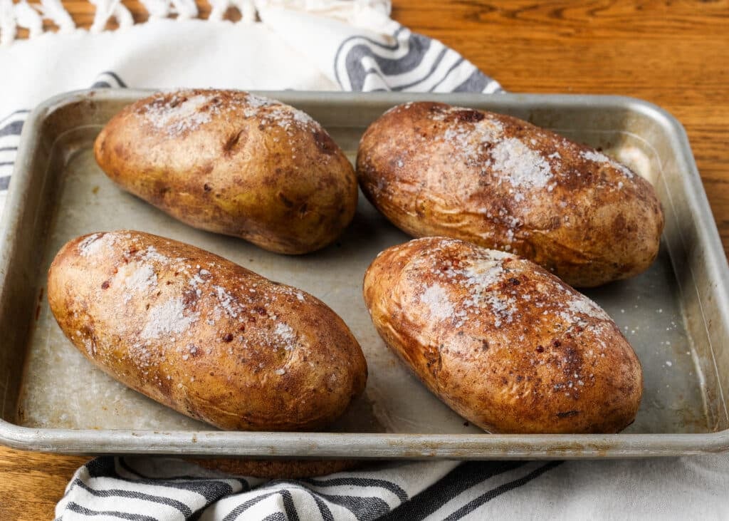 Perfectly baked potatoes on a sheet pan with crispy skins, ready to cut open and serve.
