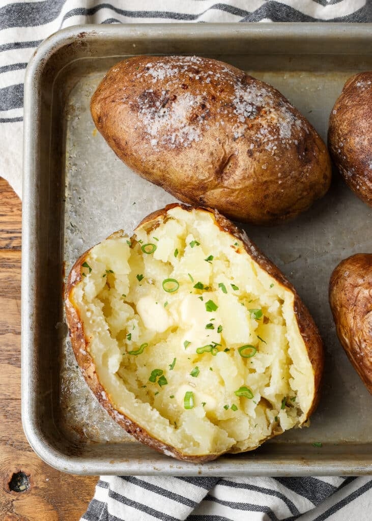 A close up on the interior of a fluffy baked potato with butter and herbs.