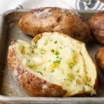 A potato on a sheet pan, topped with butter and seasonings.