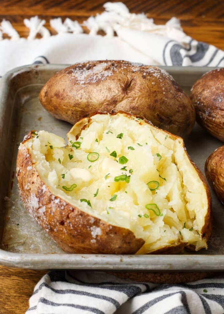 A potato on a sheet pan, topped with butter and seasonings.