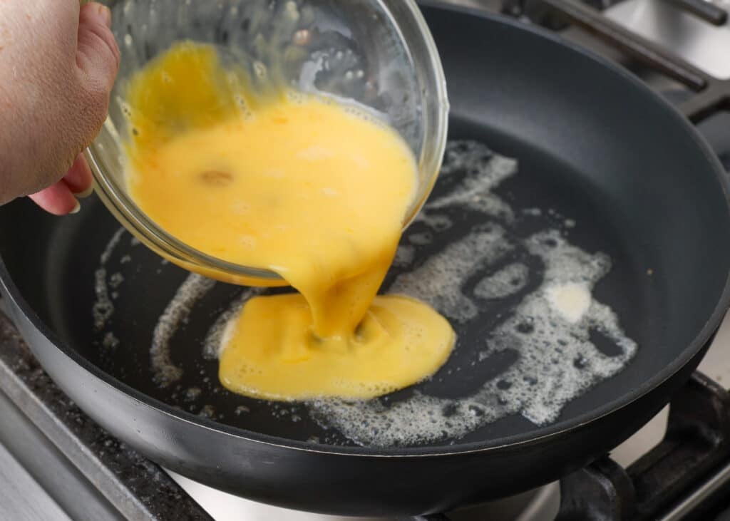 Pouring the whisked eggs into a non-stick pan.
