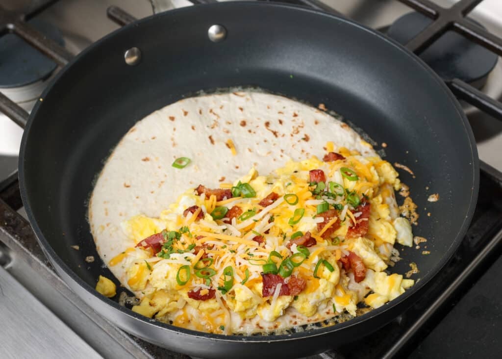 The final layer of cheese and fresh cilantro has been added to the quesadilla, ready to fold over in the pan.