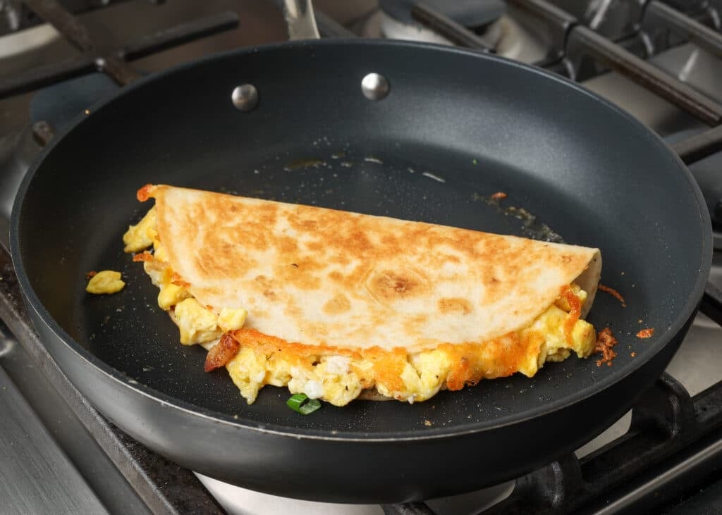 The crispy golden brown tortilla is visible on top of the quesadilla in the pan.