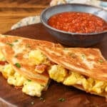 A close up of the eggs, bacon, and gooey cheese seen from the edge of the breakfast quesadilla.