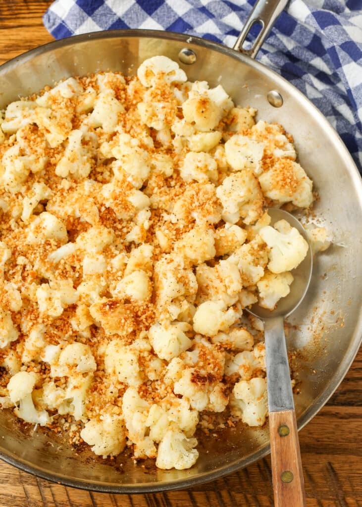 Sauteed cauliflower in skillet with serving spoon and blue napkin on table