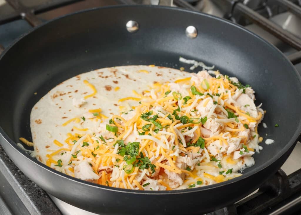 chicken, cheese, cilantro on tortilla in skillet