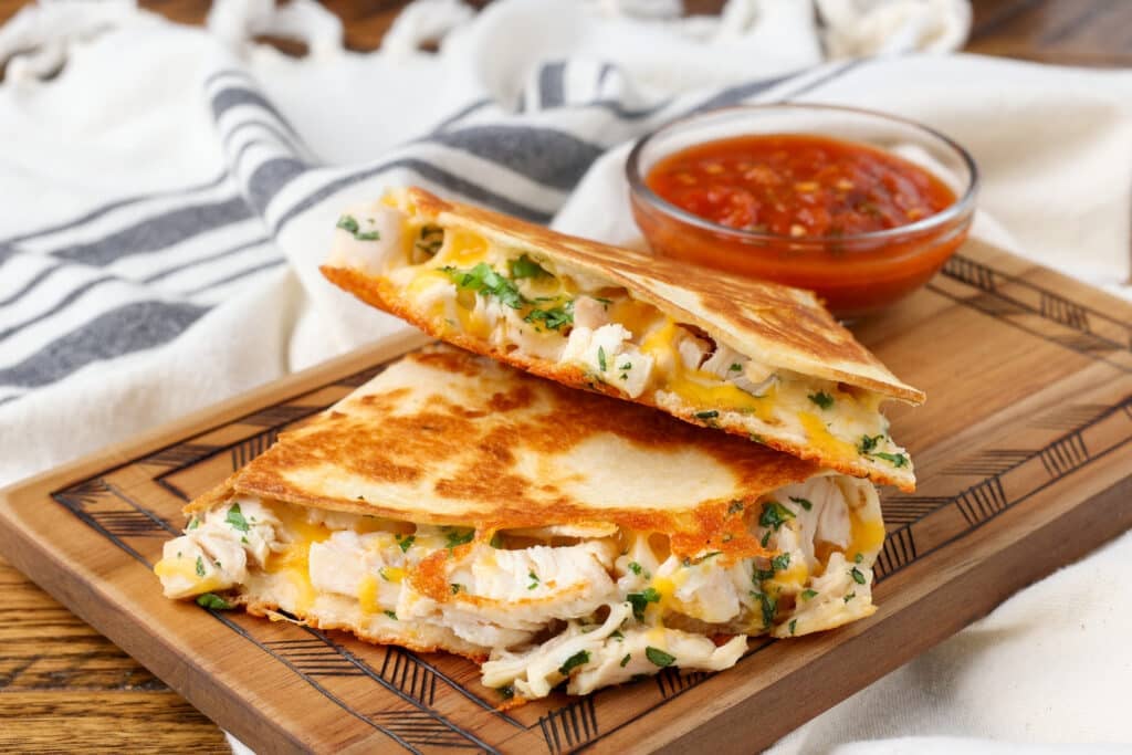 quesadillas with chicken stacked on wooden board with towel in background