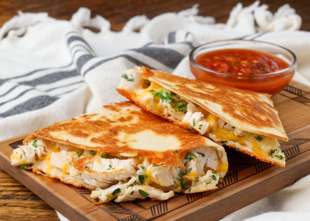 quesadilla made with chicken and cheese on board with salsa in background