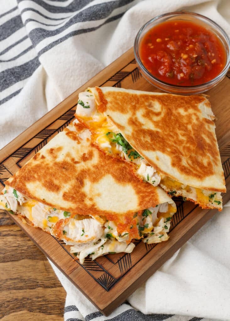 sliced chicken quesadilla on cutting board next to dish of salsa