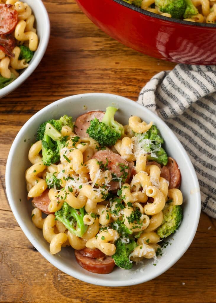 bowl of kielbasa and broccoli pasta on table with striped napkin