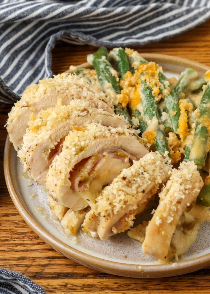 A close up of the sliced chicken cordon bleu with green chile on a plate with a striped towel visible in the background.