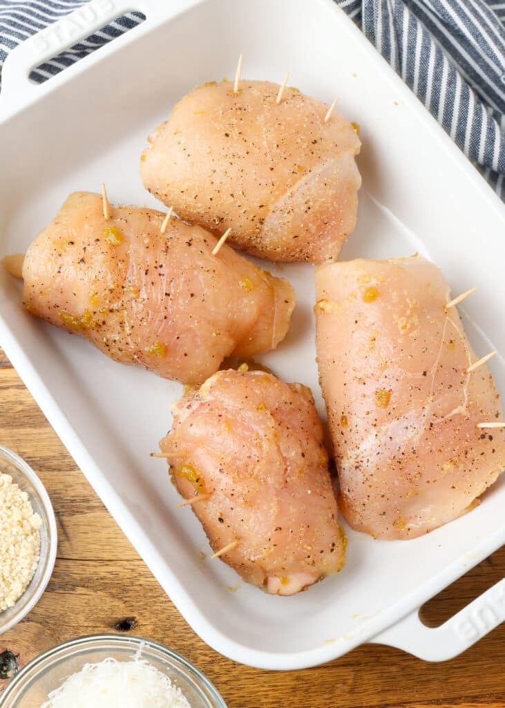 Four chicken cutlets prepared and ready to bake are in the white baking dish.