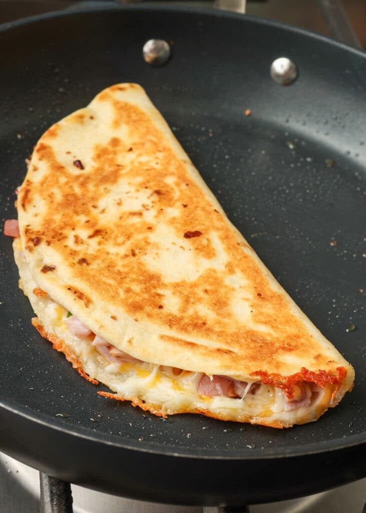 The quesadilla has been flipped in this process shot, showing the golden, crispy brown side and the cheese melting around the edge.