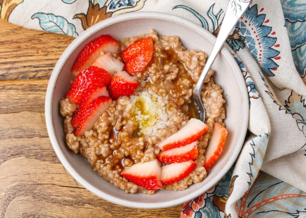 bowl of steel cut oats with berries and silver spoon on wooden table