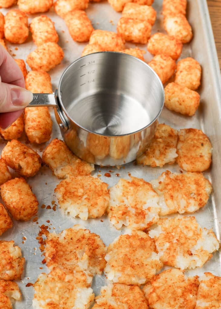 A vertically aligned action shot, showing the measuring cup pressing down on the roasted tater tots.