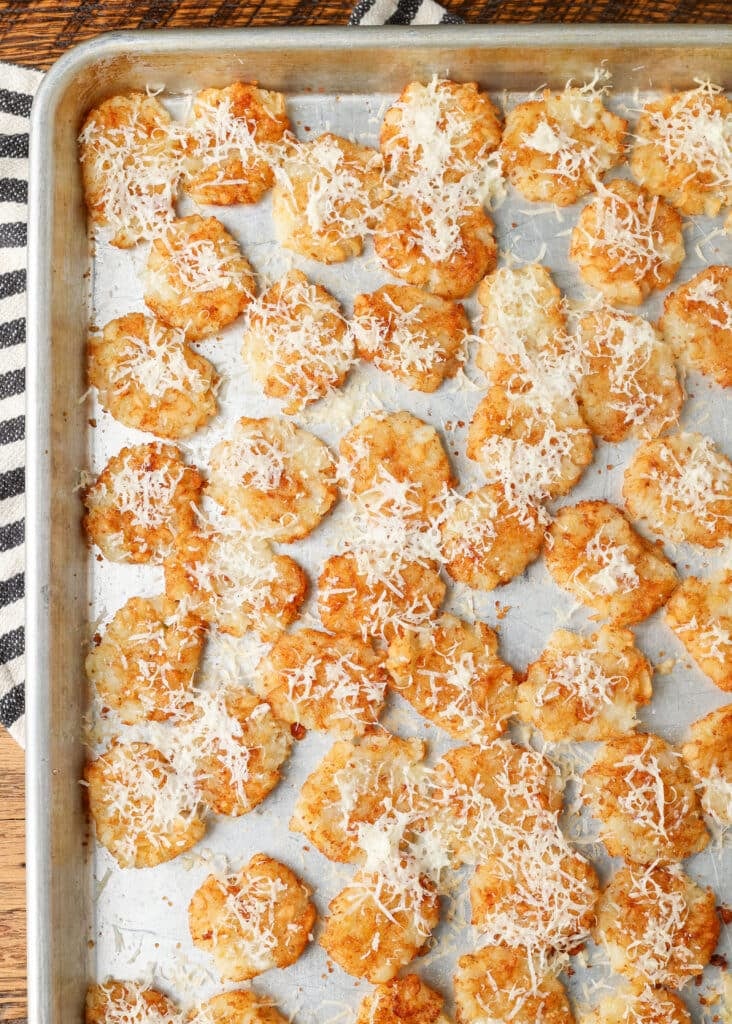A top down vertically aligned image of tater tots on a sheet pan. they have been compressed into flat discs.