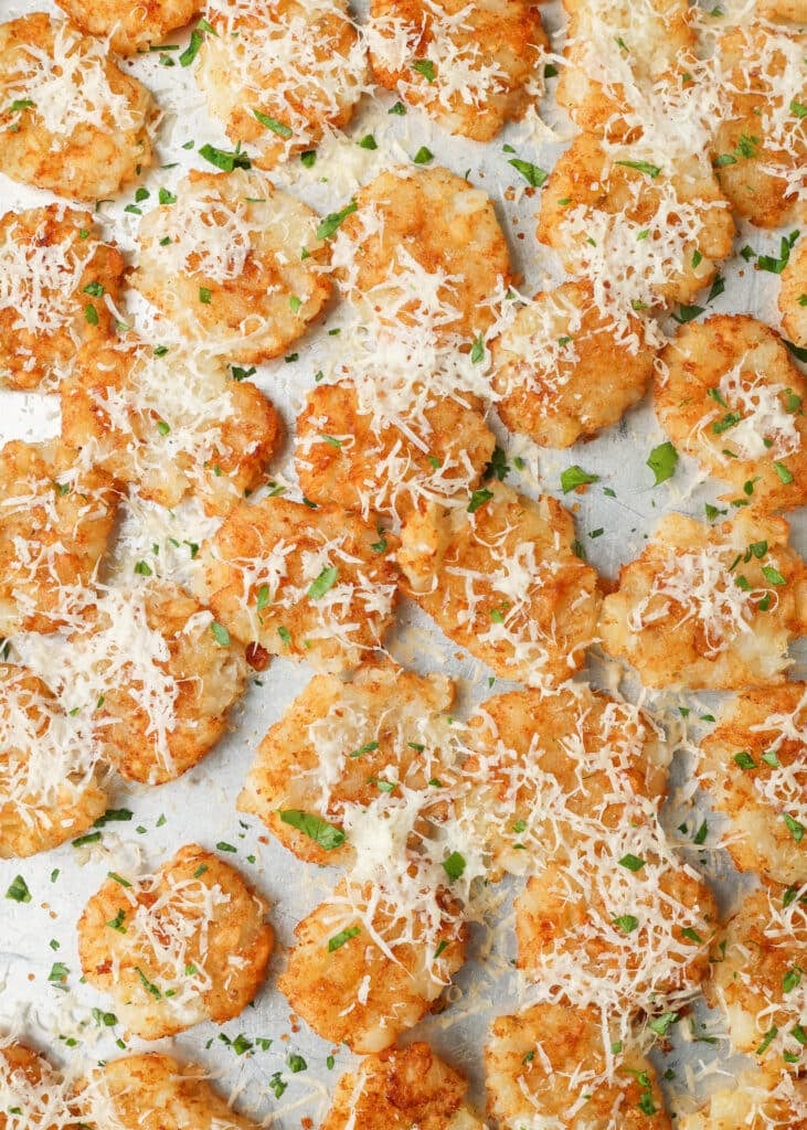 A vertically aligned top down image of a metal sheet pan covered with smashed tater tots, ready to eat.
