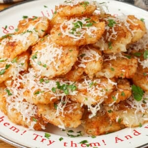 A vertically aligned photo of a white plate piled high with smashed tater tots, covered in cheese and herbs.