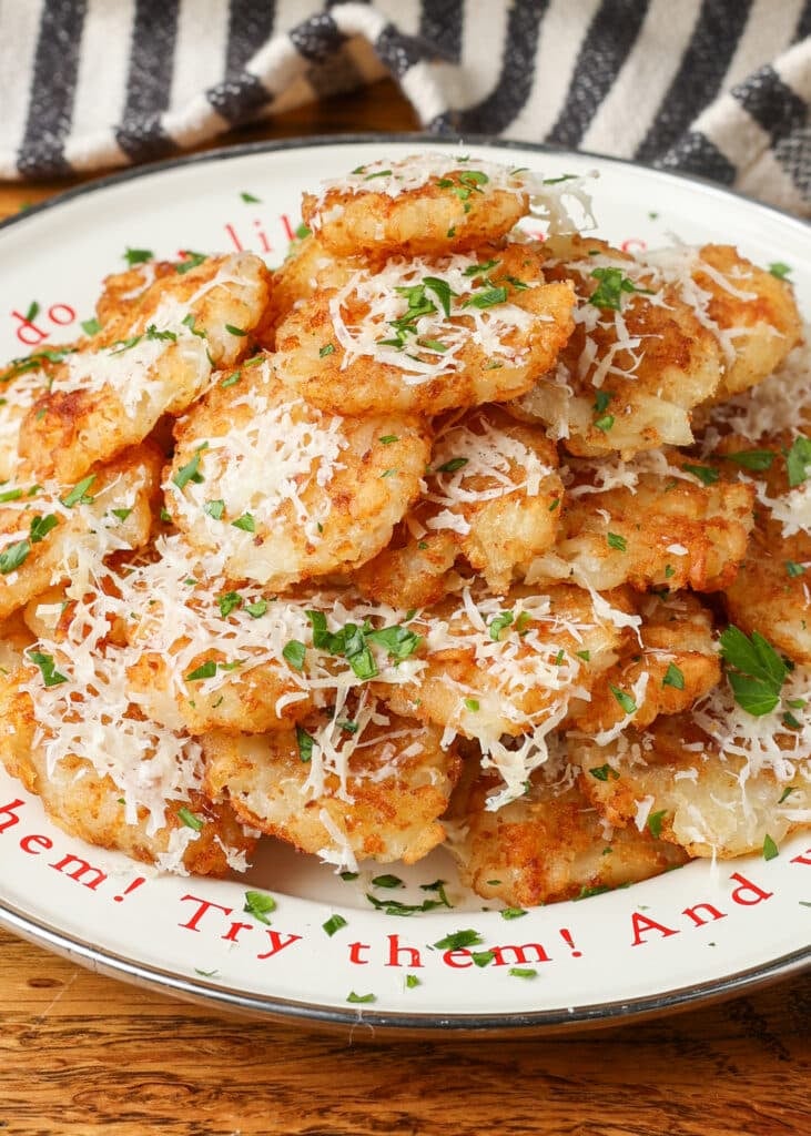A vertically aligned image of a white plate piled high with smashed tater tots, covered in cheese and herbs.