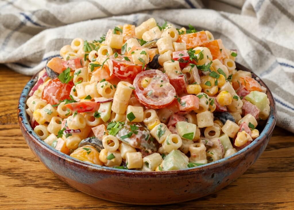 A horizontally aligned image showing a bowl of southwest pasta salad on a wooden tabletop.