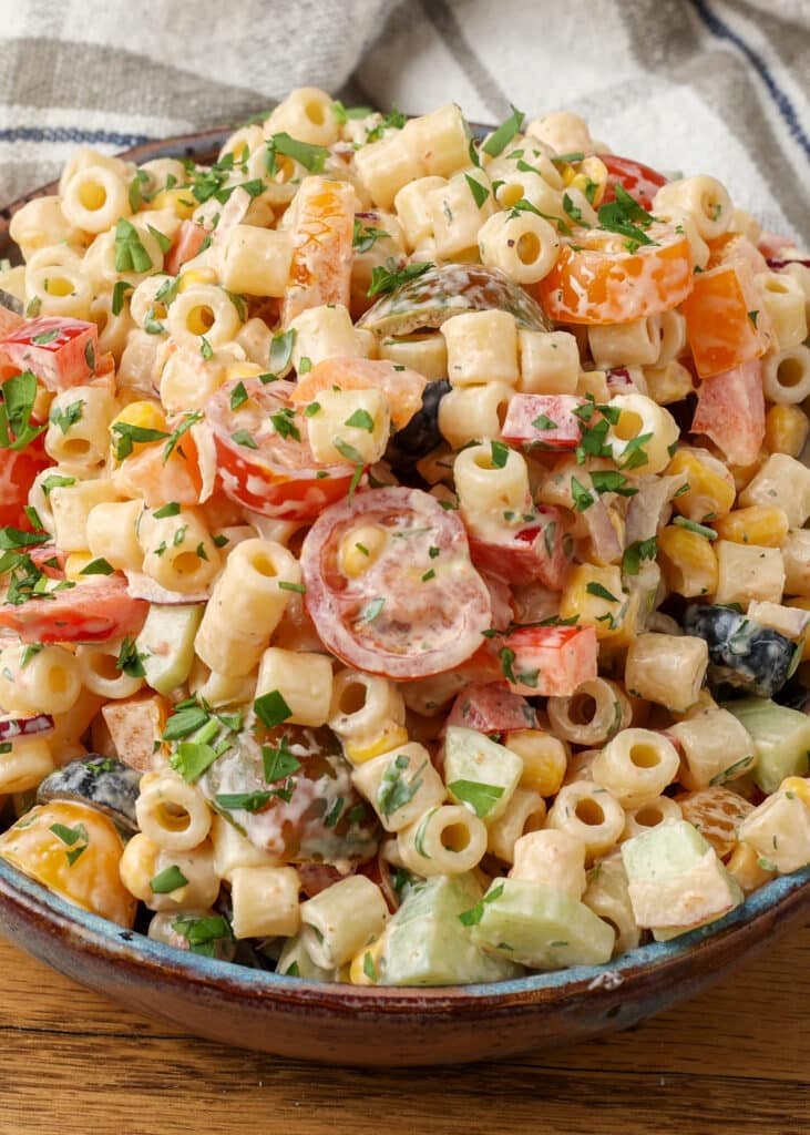 A vertically aligned close up on the pasta salad in a bowl with a grey and white tea towel in the background.