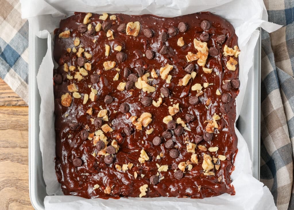 The brownie batter has been added to the pan and walnut pieces and chocolate chips are scattered over the top, ready to go into the oven.