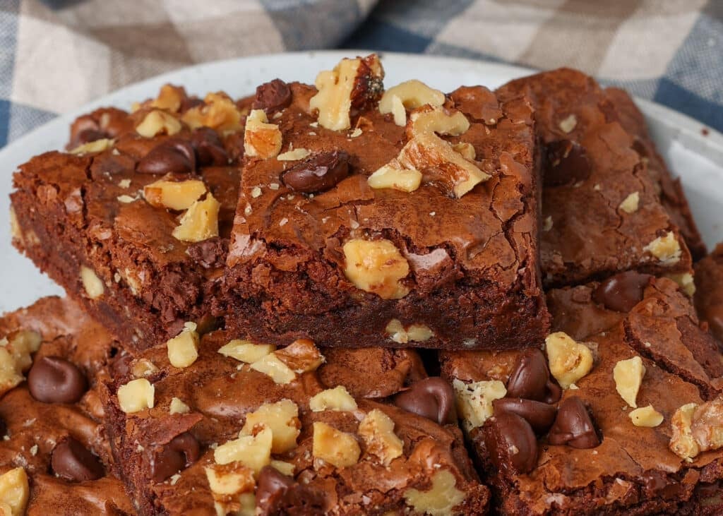 A single brownie rests atop the others, sprinkled with walnut pieces and chocolate chips.