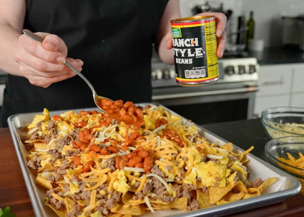 topping the nachos with eggs, sausage, and chili beans