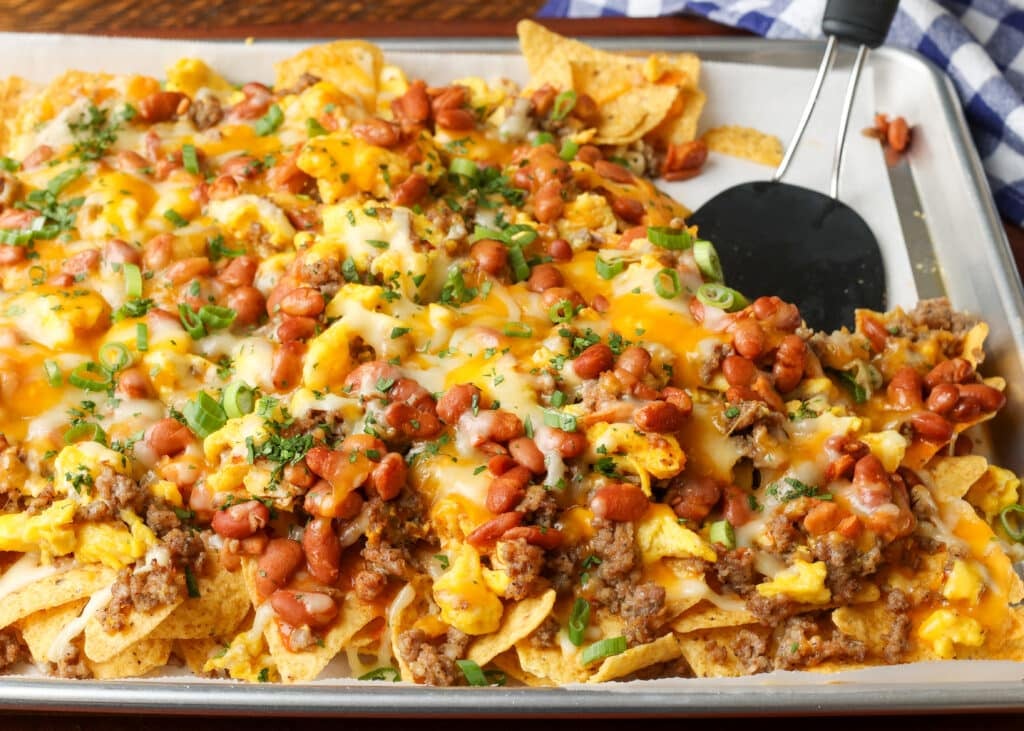 A horizontally aligned photo of a baking sheet loaded with delicious breakfast nachos.