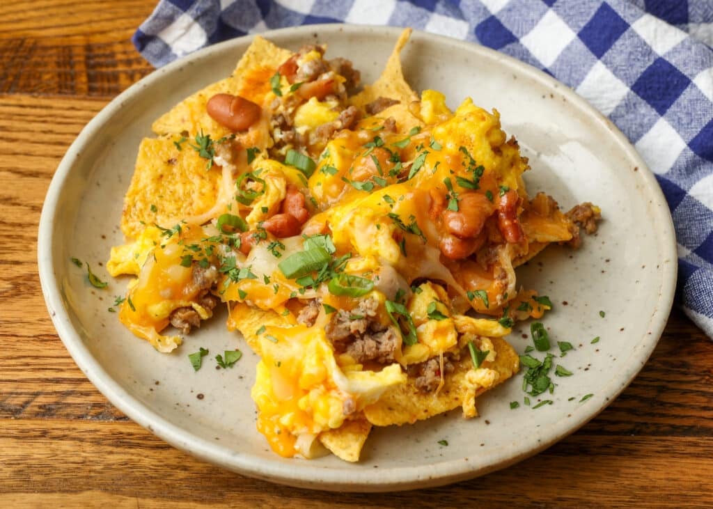 piled up nachos with sausage and egg and cheese on pottery plate on wooden table