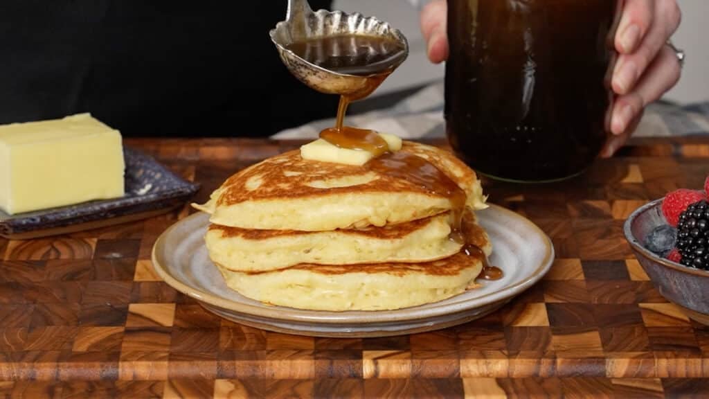 buttermilk pancakes on plate with butter and syrup poured over them