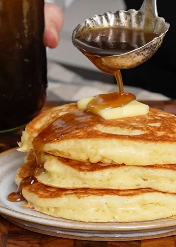 close up of stacked pancakes on plate with butter and syrup ouring over the stack
