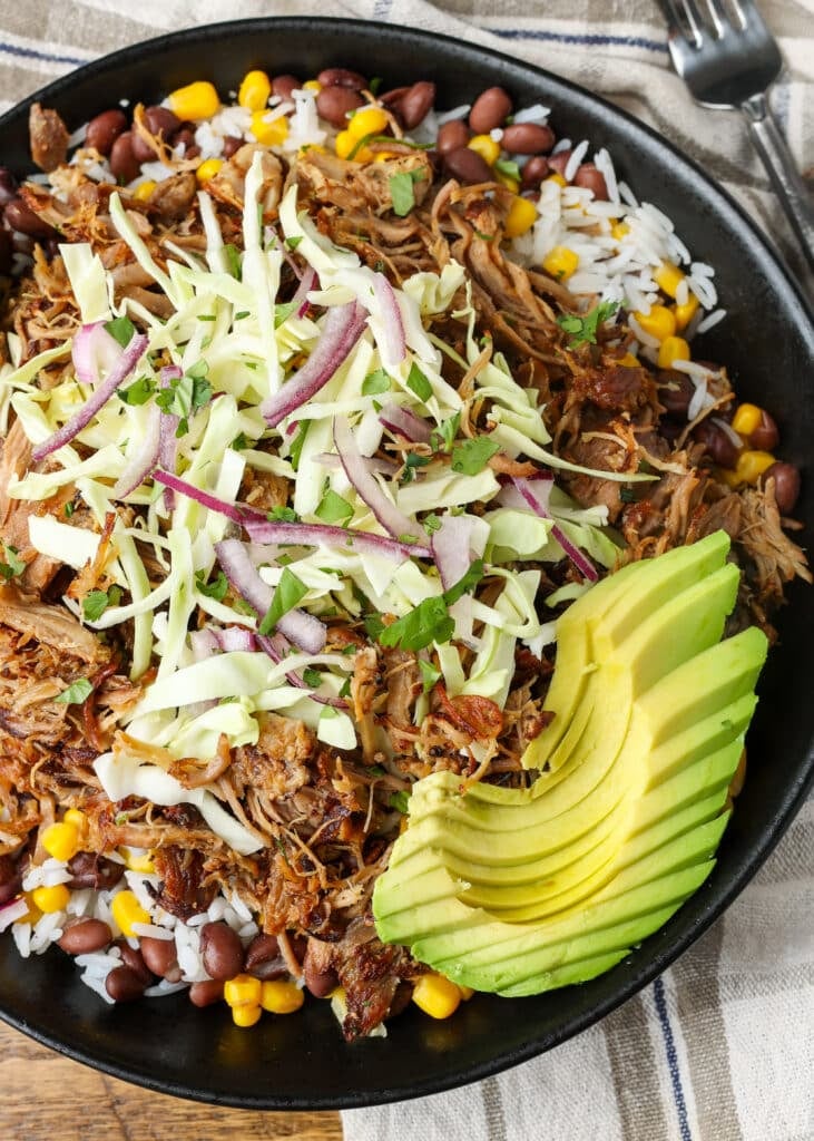 A top down image of the black bowl filled with ingredients, with half an avocado artfully sliced and fanned out on the top.