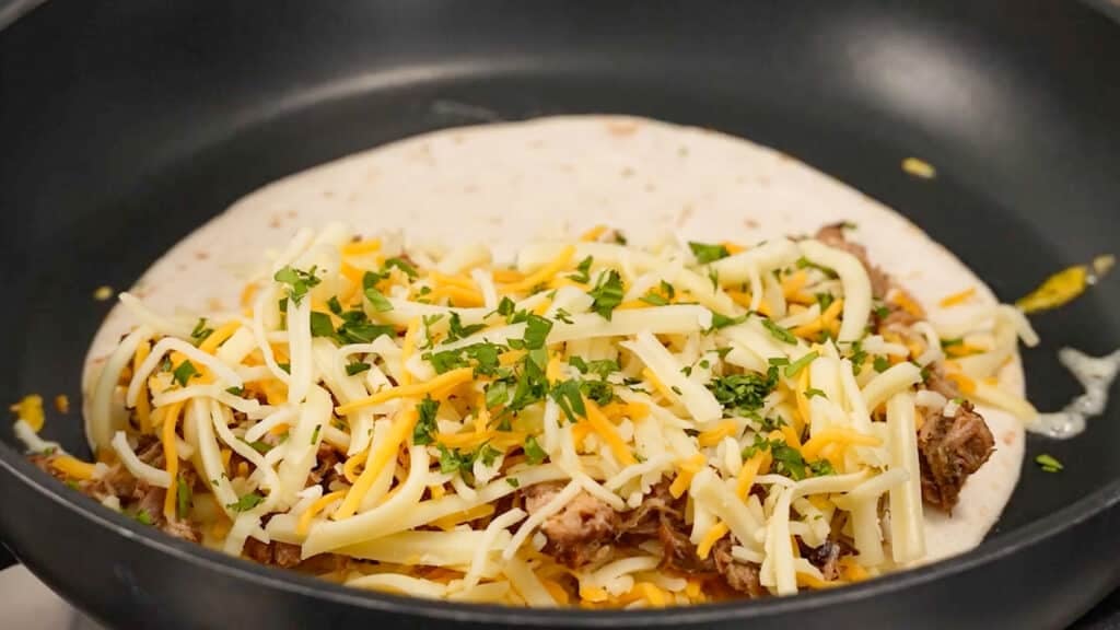 cheese, meat, cheese, and cilantro layered over tortilla in skillet