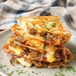 A stack of carnitas quesadilla wedges on a ceramic plate, sprinkled with cilantro.
