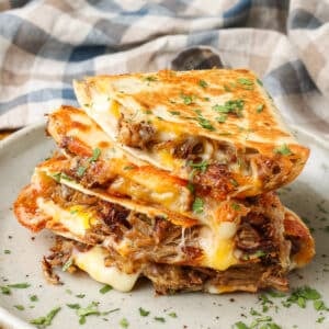 A stack of carnitas quesadilla wedges on a ceramic plate, sprinkled with cilantro.