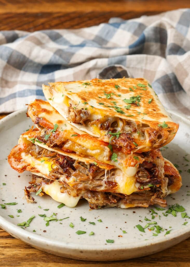 A stack of carnitas quesadilla wedges on a ceramic plate, sprinkled with cilantro.