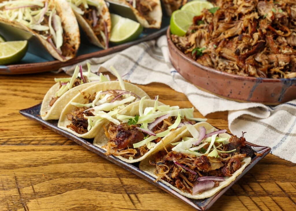 Pork carnita tacos on platter on wooden table