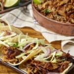 Carnitas tacos on plate next to platter of carnitas meat