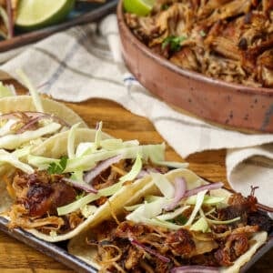 Carnitas tacos on plate next to platter of carnitas meat