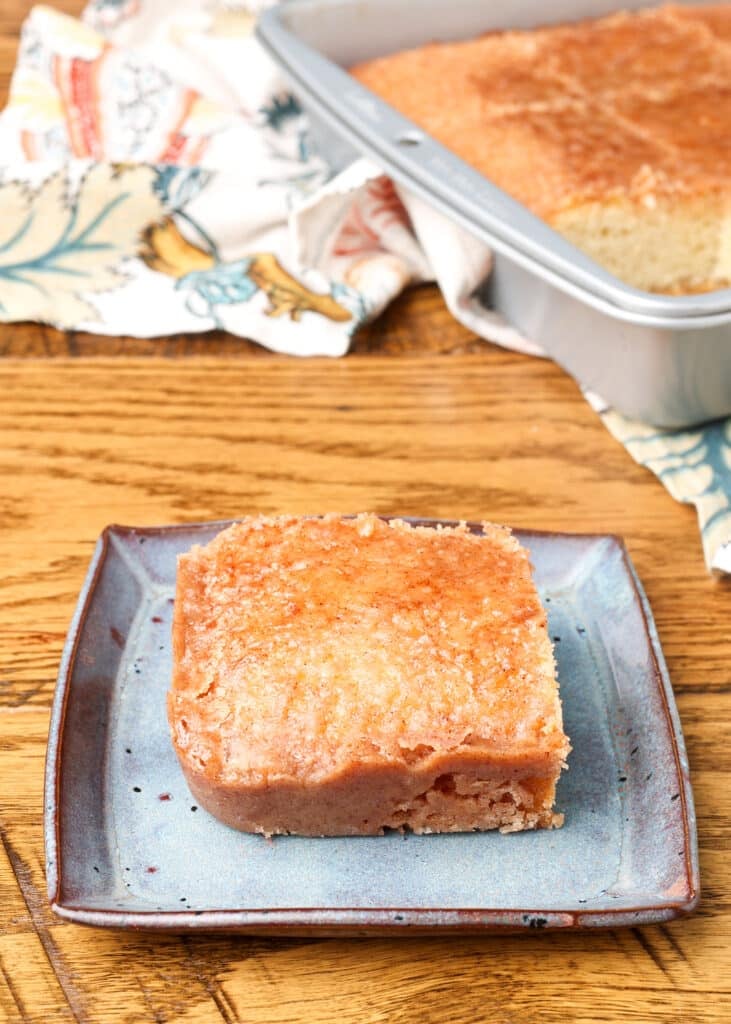 A square of cake has been placed on a plate in the foreground, with the rest of the cake visible in the pan in the background.