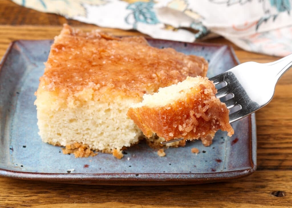 A bite of cake rests on a fork in the foreground, with a square of cake visible in the background on a blue plate.