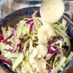 Dressing the coleslaw with a metal spoon, drizzling it over freshly shredded cabbage.
