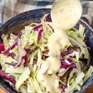 Dressing the coleslaw with a metal spoon, drizzling it over freshly shredded cabbage.